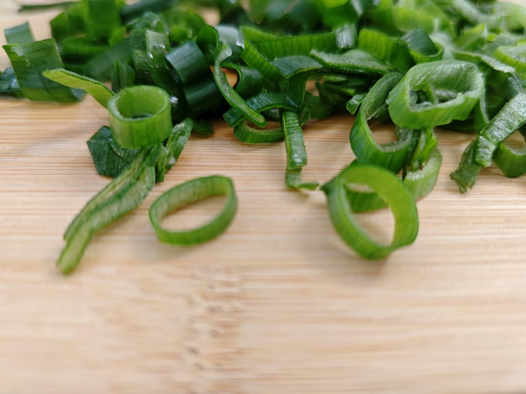 Sliced green onions on a cutting board used to add freshness and color to air fryer Pad Thai–style chicken