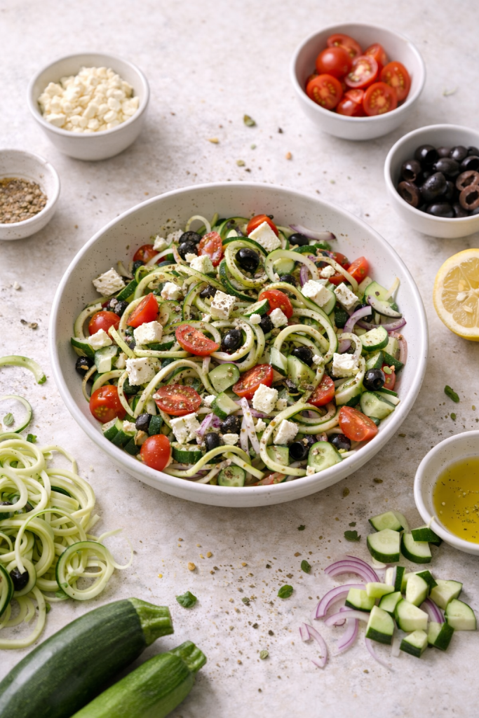 Greek-style zucchini noodle salad with feta, tomatoes, and olives served in a bowl.