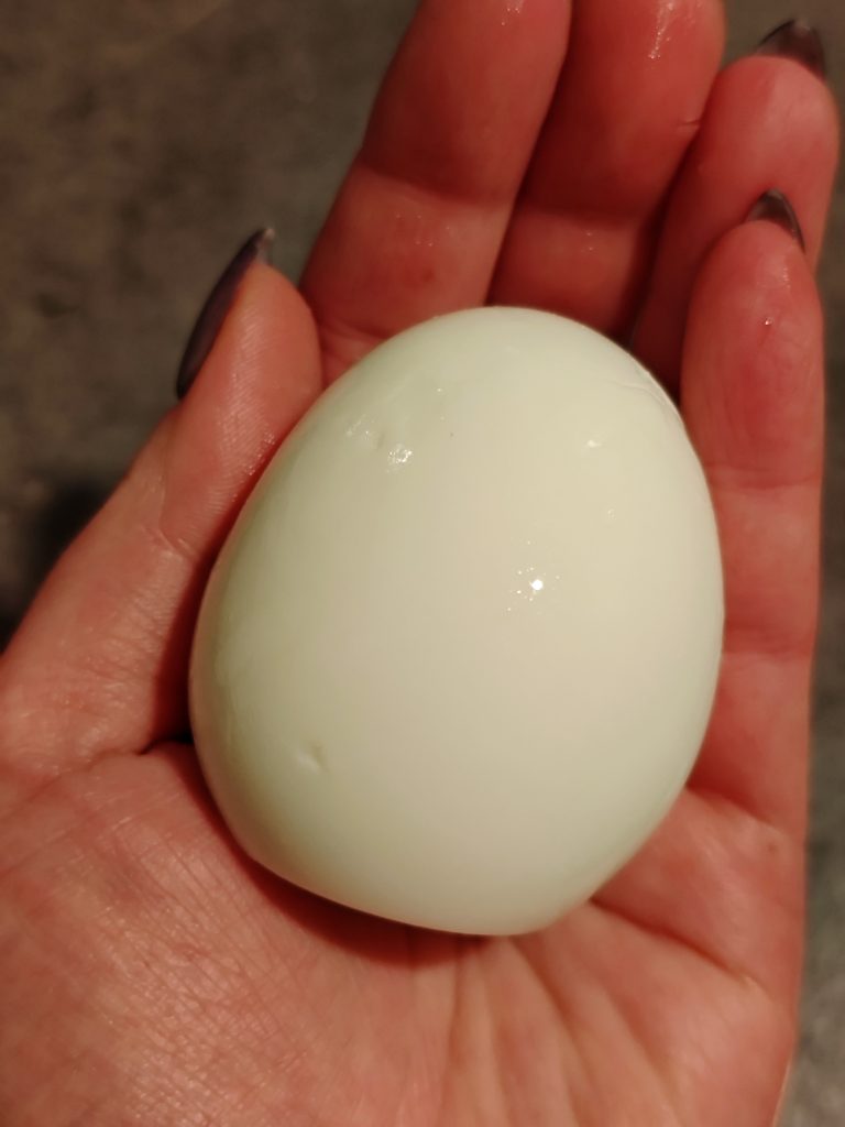 Peeled hard-boiled egg held in hand over a light kitchen background