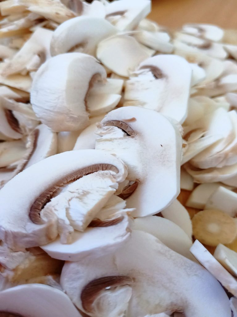 Fresh sliced mushrooms on a cutting board prepared for baked brie with mushrooms and garlic.
