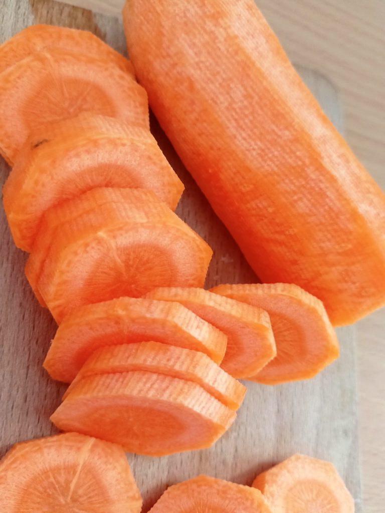 Chopped carrots on a cutting board prepared for a savory vegetable stew served with buckwheat fritters.