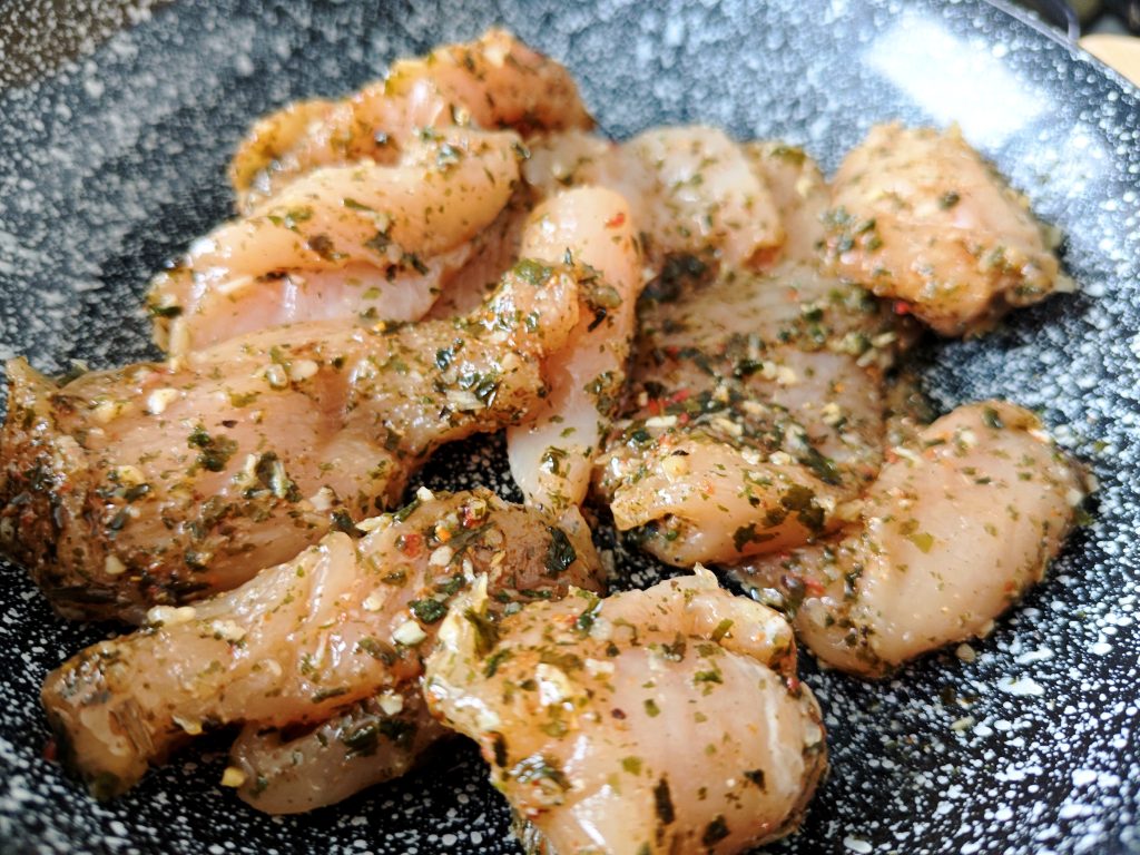 Seasoned chicken pieces cooking in a pan with visible spices