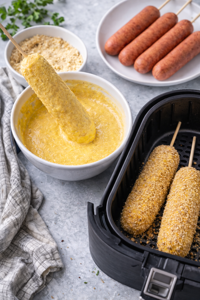 breaded corn dogs ready in air fryer basket with batter and breadcrumbs during preparation