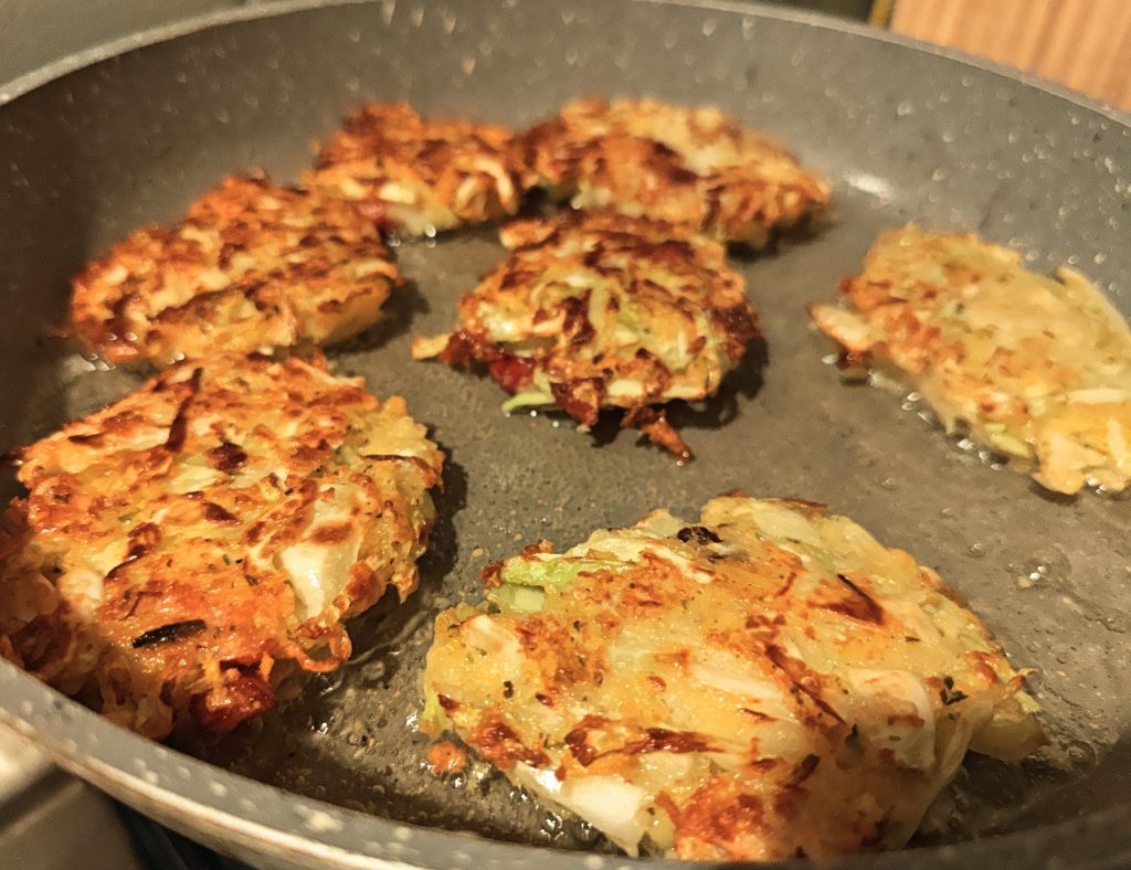 Cabbage and bacon fritters frying in a pan until golden and crispy