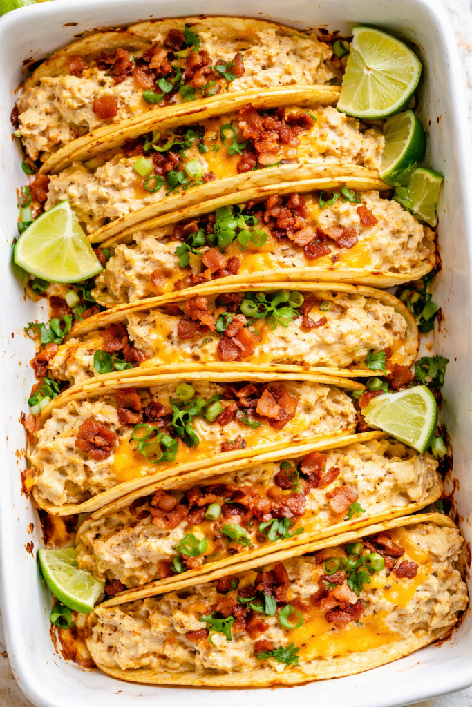Creamy baked chicken tacos recipe with shredded chicken, melted cheese, bacon, and green onions in crispy taco shells