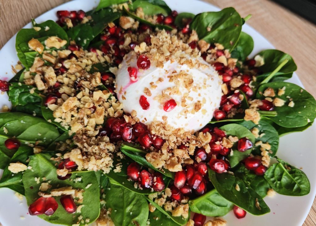 Spinach salad with burrata, pomegranate seeds, and walnuts topped with honey balsamic dressing