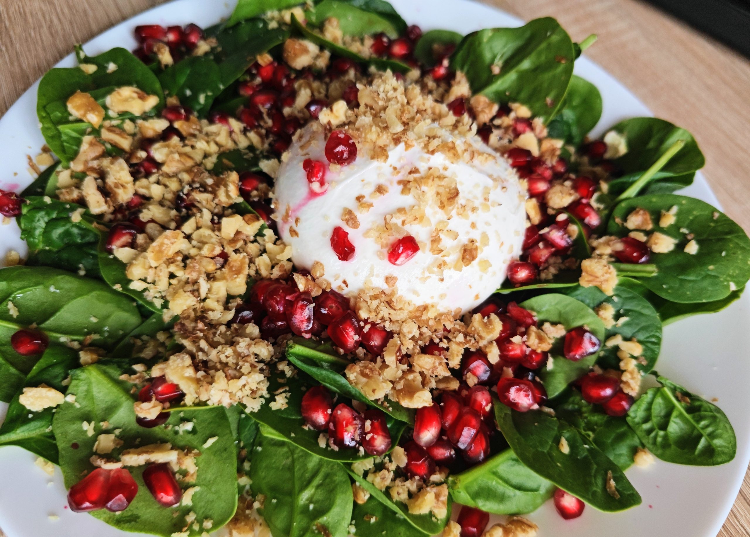 Spinach salad with burrata, pomegranate seeds, and walnuts topped with honey balsamic dressing