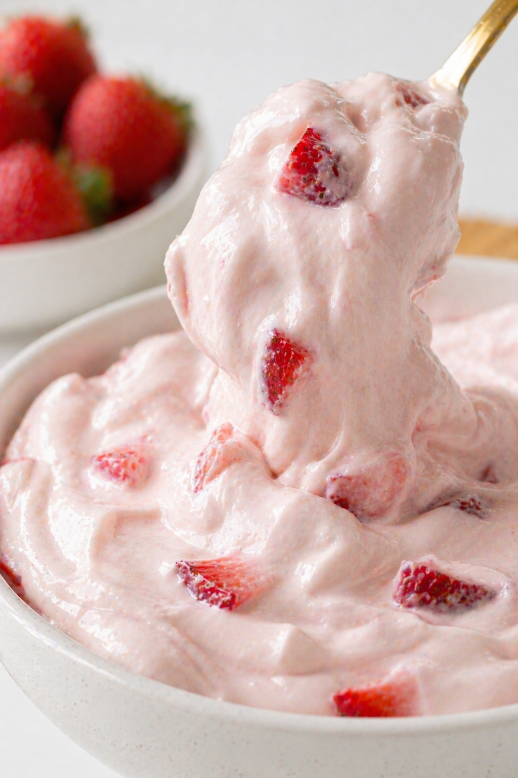 close up of strawberry cheesecake dip with smooth creamy texture and visible strawberry pieces lifted on spoon